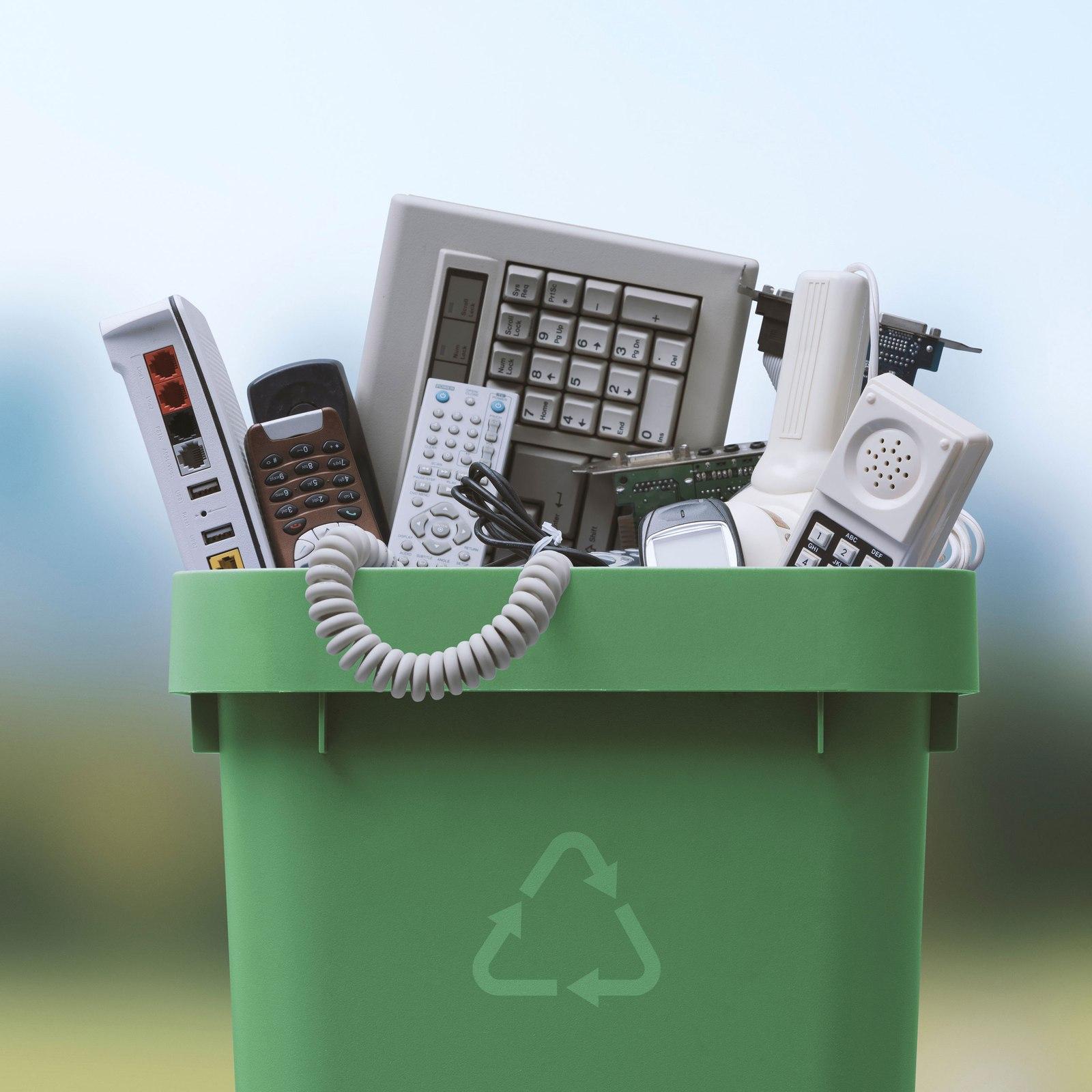 A bin overflowing with collected e-waste — keyboards, phones, remotes and circuit boards ready for recycling